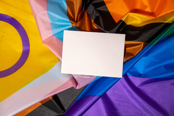 Empty paper blank on Rainbow LGBTQIA flag made from silk material. Mock up template copy space for...