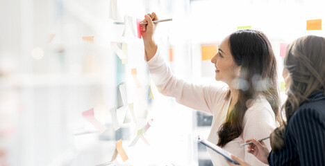 young businesswoman creative team using post it notes in glass wall to writing strategy business...