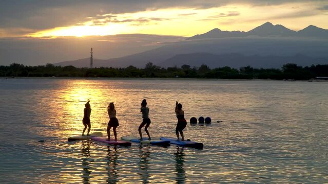 Girls do yoga on the water during sunrise. View of the volcano in Bali