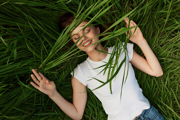 happy woman lies in high grass biting leaves with beautiful, even teeth