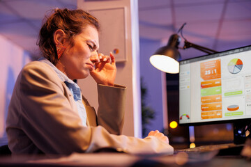 Tired businesswoman working overtime at company strategy, analyzing financial growth report on computer in startup office. Exhausted executive manager planning investment plan