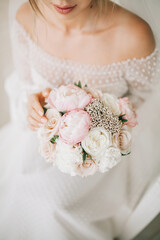 The bride in a white dress holds a delicate wedding bouquet in her hands.
