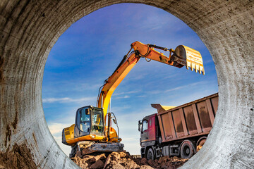 Fototapeta na wymiar A wheeled excavator loads a dump truck with soil and sand. An excavator with a high-raised bucket against a cloudy sky View from the trench. Removal of soil from a construction site or quarry.