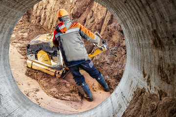 A worker compacts soil or sand with a vibrating plate in a trench at a construction site close-up. Vibratory soil compaction for laying underground utilities.