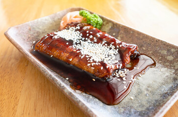 Grilled Japanese eel sprinkled with white sesame seeds in a Japanese-style square dish on a wooden table