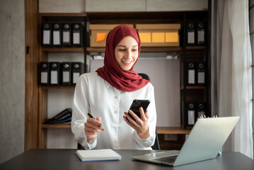 Young Arabic female entrepreneur wearing a hijab working online with a laptop at office.