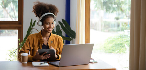 Young African woman listening music from headphones and writing note for her work idea in diary...