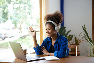Attractive young African student studying at the college library, sitting at the desk, using a laptop computer, tablet and headphones having a video chat.
