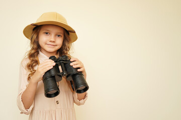 Traveler child. Child discoverer. Young researcher. Little girl in a safari hat with binoculars in her hands. Concept: search for adventure and treasure. Cute happy girl in safari clothes