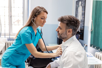 Fototapeta premium Caring Caucasian female doctor use phonendoscope examine male patient heart rate at consultation in hospital. Woman nurse or GP use stethoscope listen to man heartbeat in clinic.