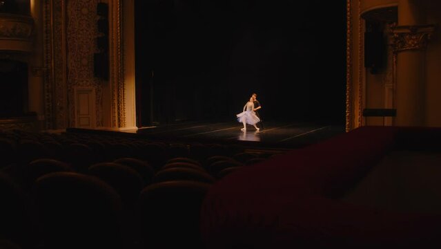 Establishing shot of ballet dancers practicing choreography on classic theater stage. Man and woman prepare theatrical performance. Shooting from spectator seat. Dramatic lighting. Full shot of stage.
