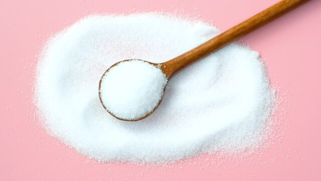 Erythritol in a wooden spoon on a pink background top view close-up.