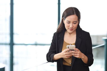 Portrait of confident young asian businesswoman researching and planning work with happy smiling face while using smart mobile phone at business meeting in modern office building and city background