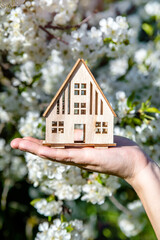 The girl holds the house symbol against the background of blossoming cherry
