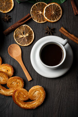 Overhead view of puff pastry sweets with cup of coffee, dried oranges and cinnamon sticks, vertical, with copy space