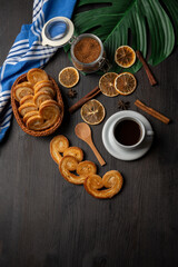 Top view of puff pastry sweets with cup of coffee, dried oranges, brown sugar and blue cloth, vertical, with copy space
