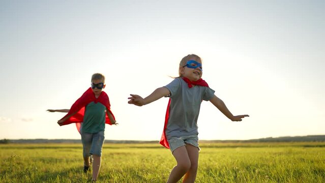 Happy children play superheroes in the open field of the park. Children in superhero red capes run across a green field. Happy dream play.Run with your dream pet. child dream concept