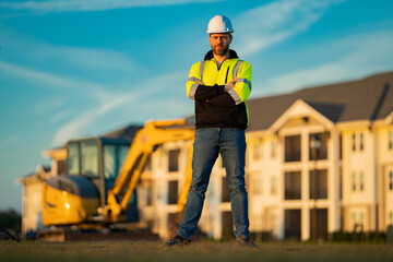 Worker in helmet on site construction. Excavator bulldozer male worker. Construction driver worker with excavator on the background. Construction worker with tractor or construction at building.