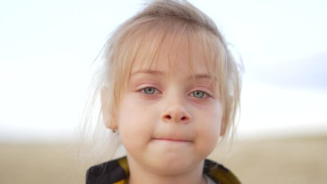 Close-up portrait of cute fair-haired girl. child looks into camera lens. One baby girl with blond hair looks forward into camera. Cute little girl face closeup