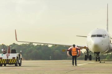 Fototapeta na wymiar Ground Crew in the signal vest. Aviation Marshall or Supervisor meets passenger airplane at the airport. Aircraft is taxiing to the parking place. Apron movement control officer in safety vest parking