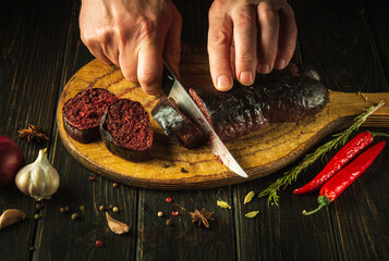 Chef's hands with a knife cut blood sausage on a kitchen cutting board. Cooking a national dish...