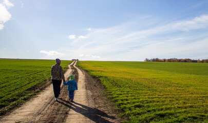 a woman with a child walk along the road in a green field