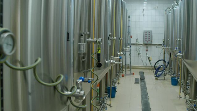 Pan shot of glass vial with gas bubbles seeping out of valve through liquid, and two rows of bright beer tanks in operation at independent craft brewery