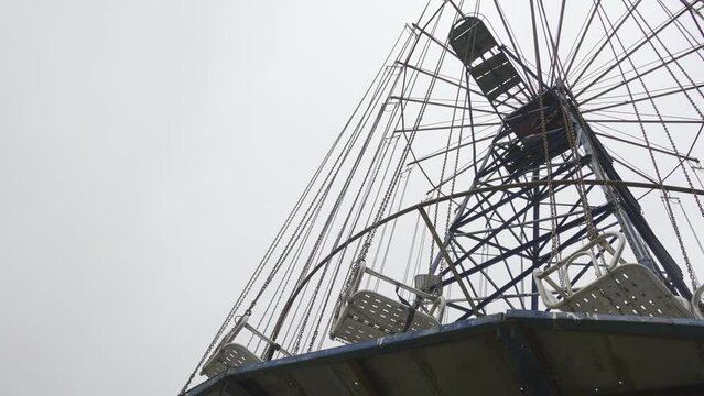 Abandoned old carousels in form of seats and chains rotating in circle sway in wind against background of overcast sky of clouds;. Old abandoned attractions. Horror and Horror Film.