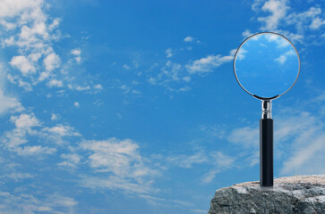 Magnifying glass on rock mountain over blue sky with white clouds, Business analyzing concept