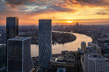 View through the modern skyscrapers of Canary Wharf of the urban London skyline and Thames river during sunset time, England