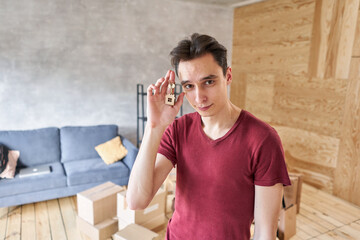 Fototapeta na wymiar Young single man holding key to new apartment on hand. Home owner Male house buyer. Moving into own flat. Mortgage purchase concept.