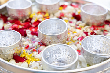 Silver water dipper with jasmines and rose petals floating in scented water of silver bowl. Colorful flowers pedestal for Songkran water festival in Thailand.