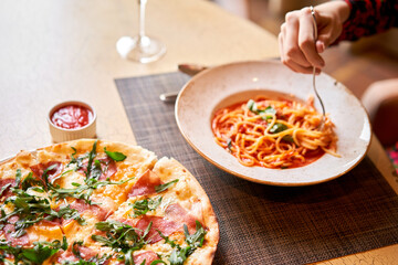 Woman eats Italian pasta with tomato, meat. Close-up spaghetti Bolognese wind it around a fork with a spoon. Parmesan cheese