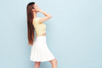 Image portrait of optimistic woman in yellow  t-shirt and white skirt. Carefree stylish model with long hair. Smiling female posing in studio. Isolated. Looks delightful and cute. Slim