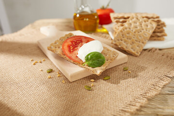 Fototapeta na wymiar brown crispbreads with tomatoes and cheese on a wooden board. healthy snack with cereal bread. breakfast on a sunny day. crispy bread stuffed with vegetables