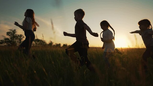Active happy family. Group of kid run together across field at sunset.Team of kid active games in nature.Silhouette of happy children outdoors in park.Kid child run on green grass.Children family play