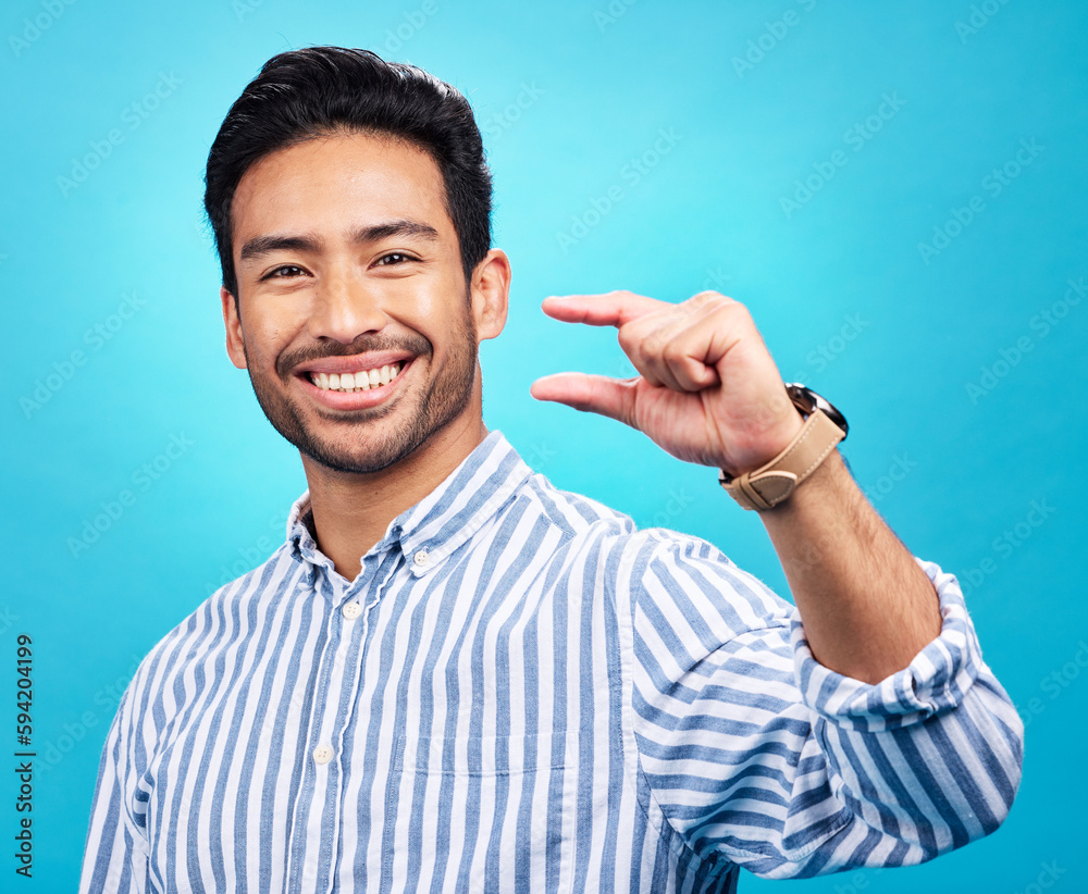 Poster Small, hand and gesture of a man portrait with a smile in studio showing a tiny measurement. Isolated, blue background and Asian model with happiness, positive opinion and hands show of pinch size