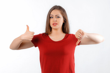 Fototapeta premium Photo of young woman showing fingers thumb-up thumb-down advert bad quality choice, frowns face in discontent, dressed in red t shirt, standing over white background