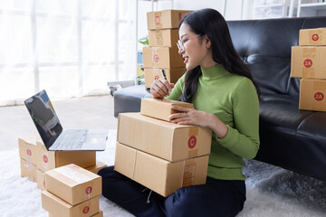 Startup SME small business entrepreneur of freelance Asian woman wearing apron using laptop and box to receive and review orders online to prepare to pack sell to customers, online sme business ideas.