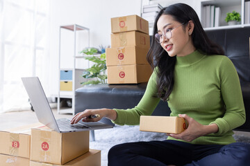 Startup SME small business entrepreneur of freelance Asian woman wearing apron using laptop and box to receive and review orders online to prepare to pack sell to customers, online sme business ideas.