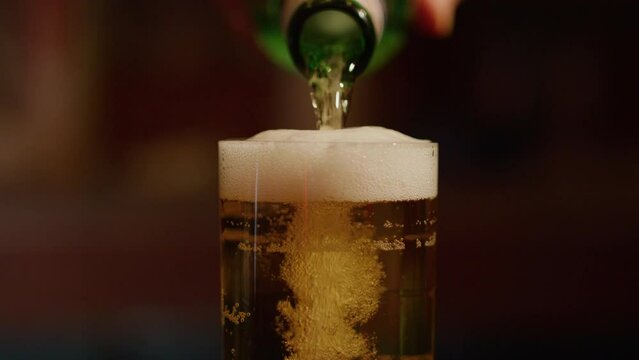 Pouring beer into glass in slowmo and rising foam flowing over