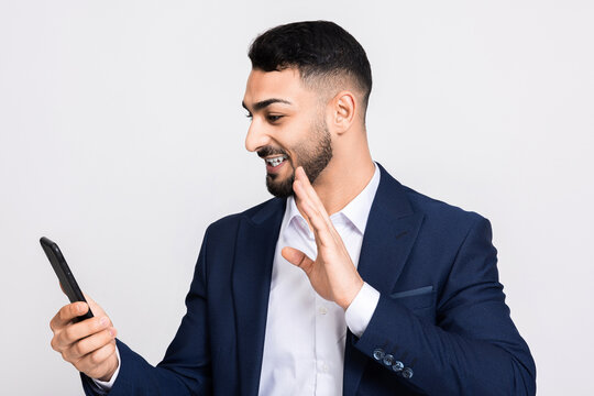 Happy successful man in buisness suit holding cellphone in hand taking picture selfie over grey background in studio isolated while shooting process.