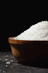 Coarse white salt in a wooden bowl on the black background