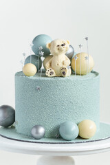 Cake with blue or turquoise velvet cream coating with teddy bear on top. Birthday cake for a little baby with chocolate turquoise and silver spheres on the white background. One year old celebration.