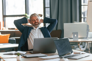 Taking a break, satisfied with success. Senior businessman is working in the office