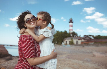 little girl of 5 years kisses happy mother in white and red dresses on beach