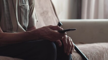 hands of an elderly man switching programs by pressing the buttons of the tv remote, sitting on the couch. leisure pensioner, real elderly people.lifestyle.nursing home