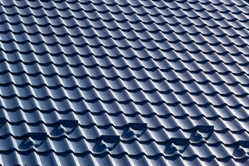 The roof of a house covered with sheets of blue metal tiles against the background of the sky on a summer day. Business selling building materials or repairing house roofs