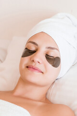 Beautiful young woman with under eye patches in bathrobe lying in bed. Happy girl taking care of herself. Beauty skincare and wellness morning concept
