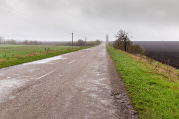 Fototapeta na wymiar Rural asphalt road among the farmlands in overcast rainy day